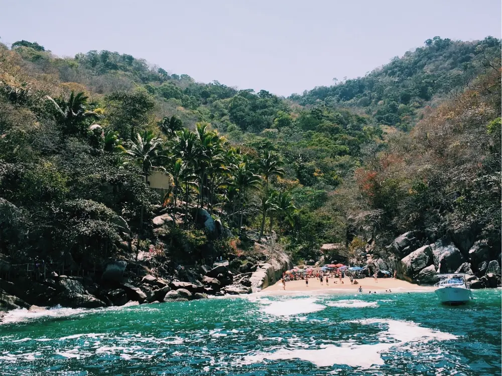 Playa escondida entre palmeras y cerros vista desde una lancha en Puerto Vallarta, referencia al contenido lifestyle de playa en Instagram México